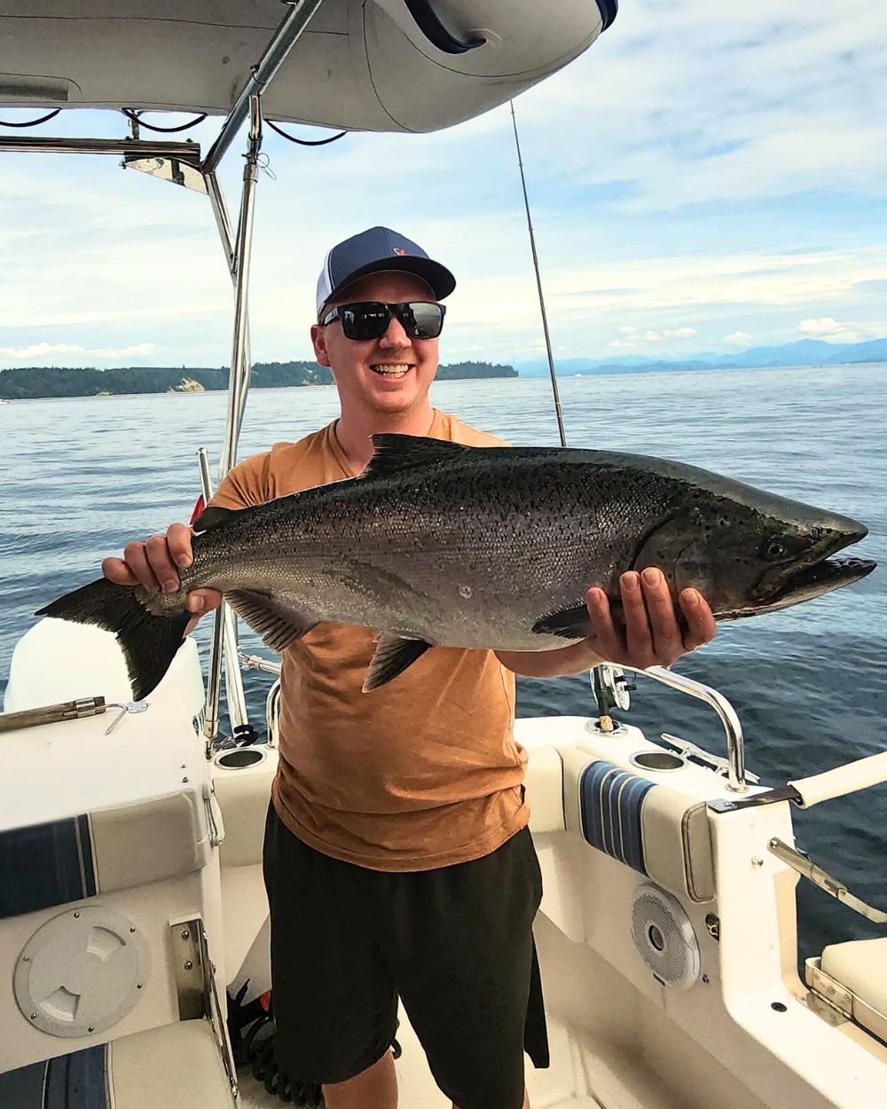 Man smiling as he presents a fresh caught fish during a beautiful day on the lake. He loves Island Life Expeditions' fishing charters.