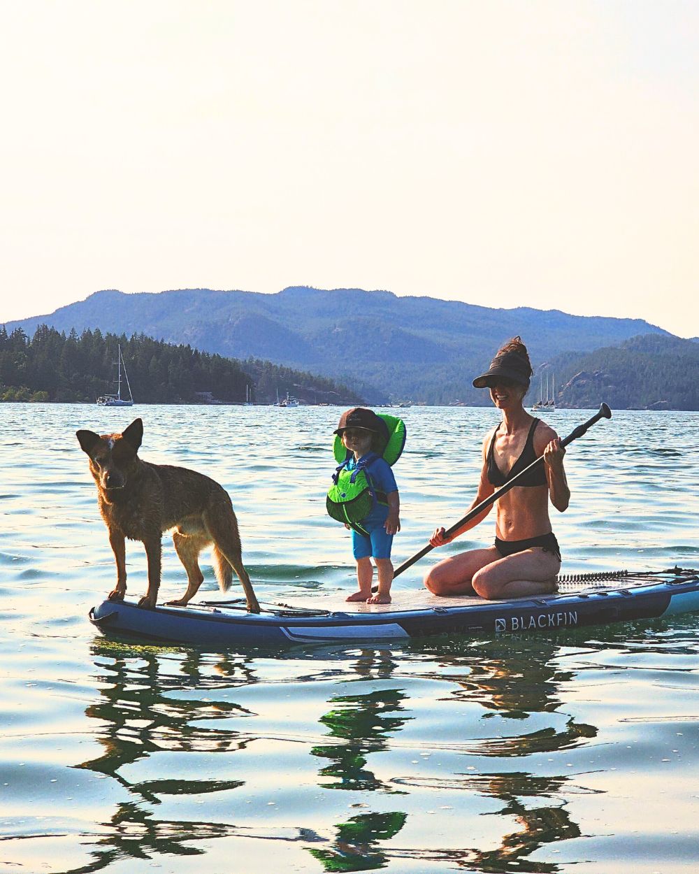 A family photo of a mother, her son, and their dog enjoying a boat supported SUP/kayak tour on the ocean of British Columbia.