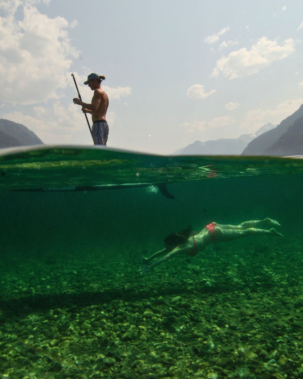A young man paddling on his standup paddle board with a woman in a pink bikini swimming underneath him in the ocean. Paddle Board Touring The perfect getaway for nature lovers. Paddle through the scenic beauty of Desolation Sound, BC. Discover BC’s stunning islands with Island Life Expeditions.